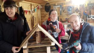 Two women and a man standing by the bug hotel they have made using pallet wood and other recycled wood.