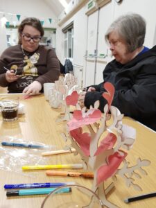 Two ladies sat at a table doing come crafts.