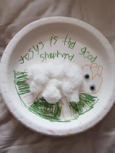 A paper plate with a sheep made from cotton wool and the words "Jesus is the good Shepherd"